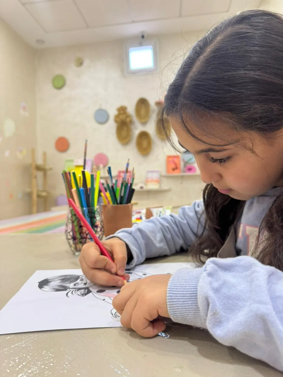 Child coloring an illustration sheet with colored pencils at Live It Maghribi kids atelier in Agadir