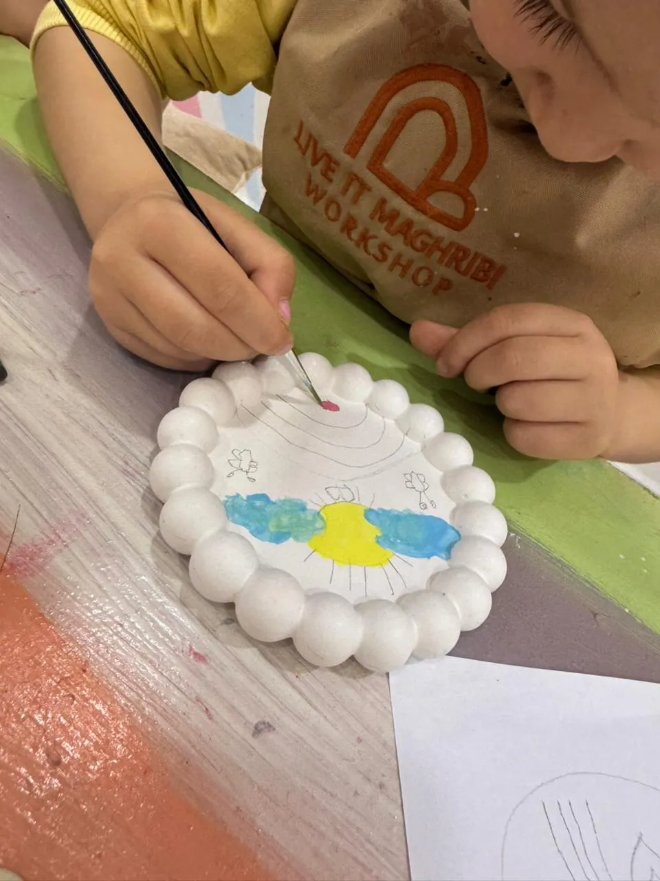 Child painting a cast plaster dish in the Live It Maghribi kids creative pack at Agadir